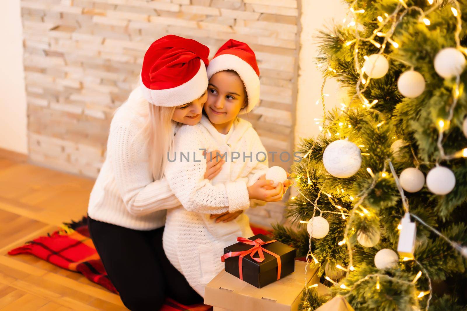 Merry Christmas and Happy Holidays Mom and daughter decorate the Christmas tree in room. Loving family indoors. by Andelov13