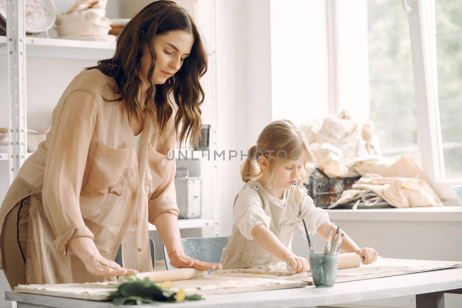 Woman and girl kneading clay. Family make art product at table in pottery workshop. Mother with daughter.