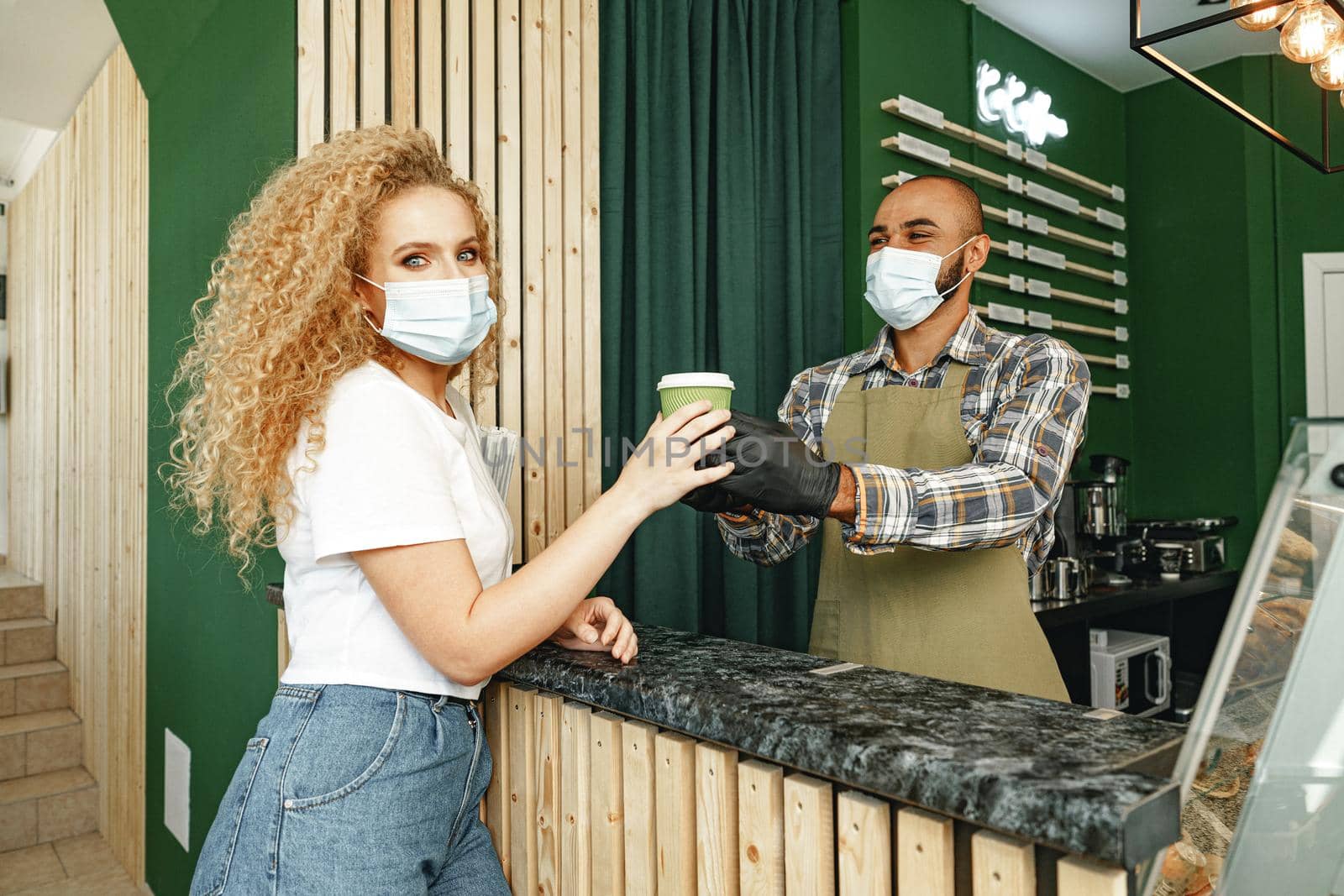 Male coffee shop worker giving ready order to the client wearing face mask, coronavirus concept