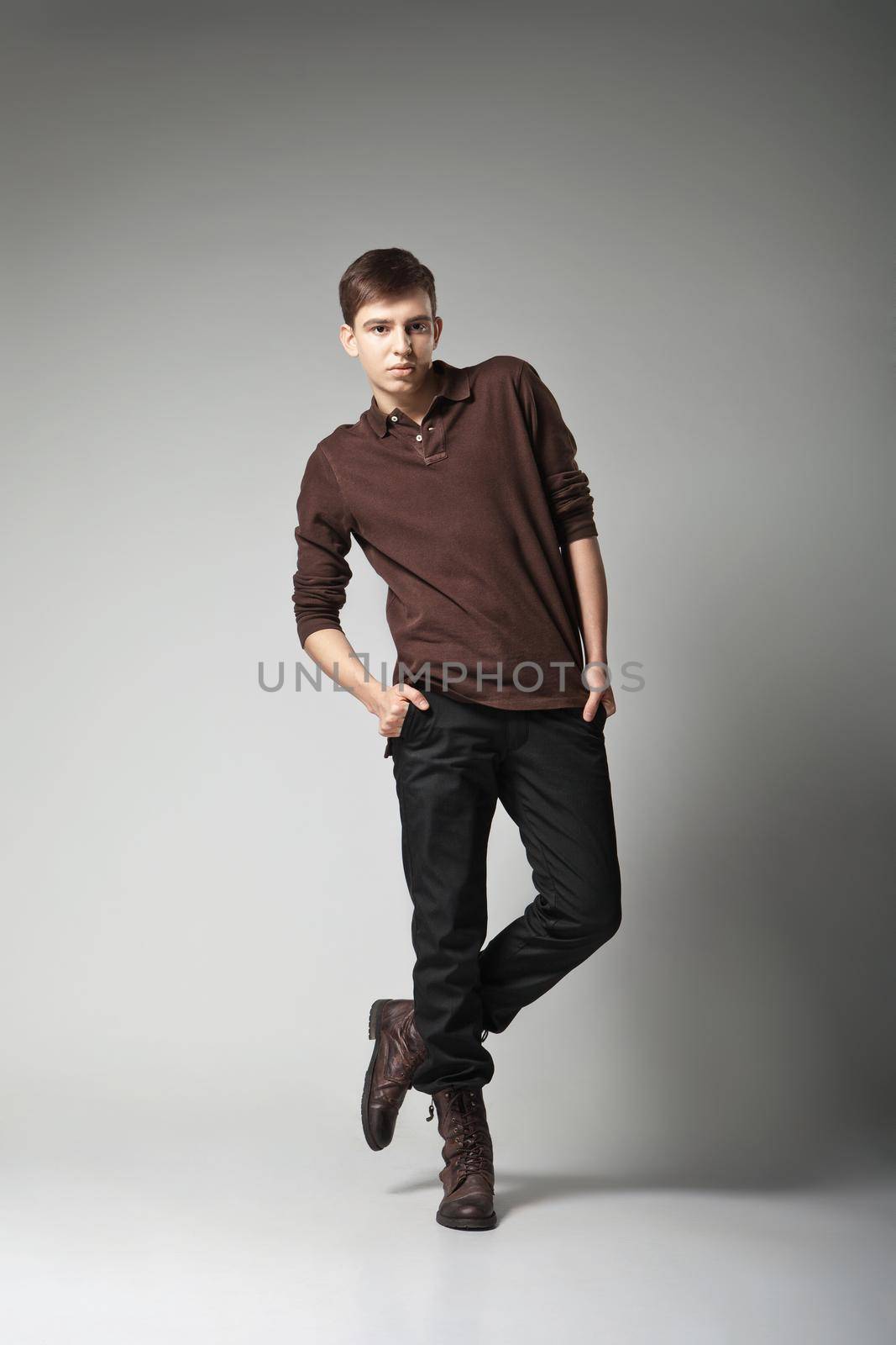 Young male fashion model posing in a casual outfit on grey background