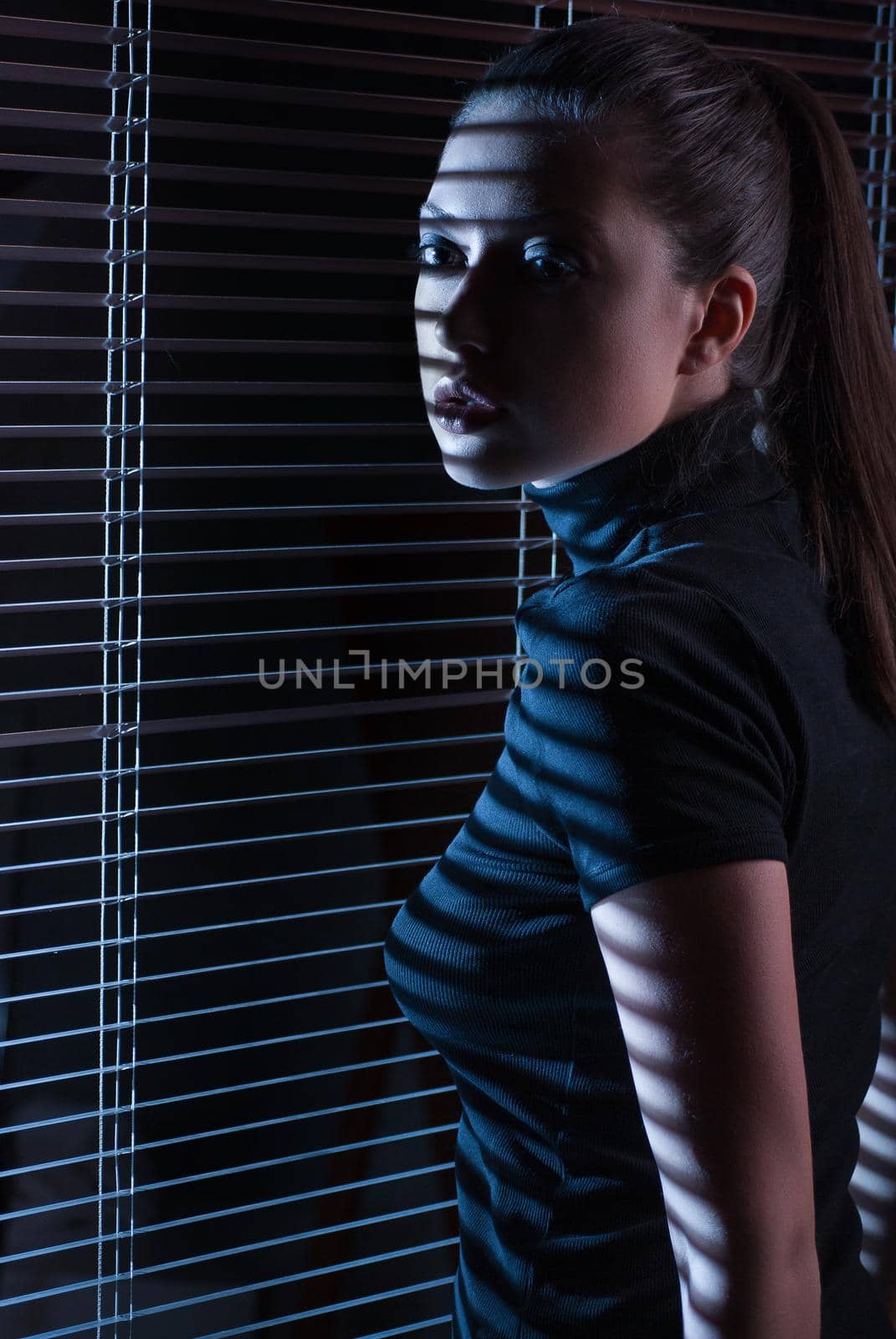 Sexy woman in black dress with jalousie looking through the window with jalousie