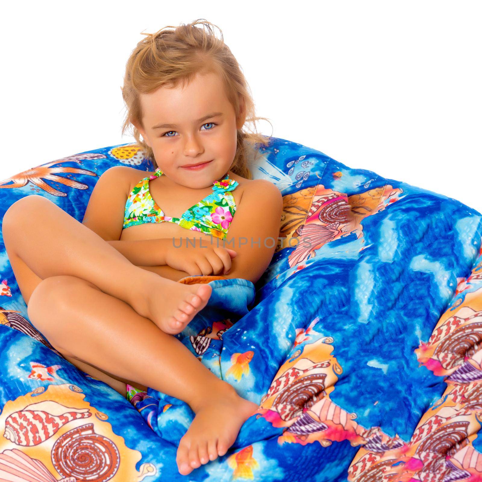 A nice little, tanned girl in a swimsuit resting on a soft pillow. The concept of summer family vacation at sea, happy childhood. Isolated on white background.