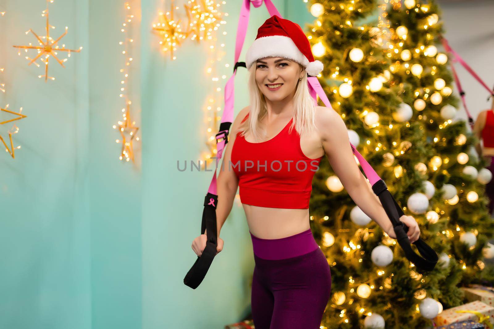 A young woman in santa claus hat holds a strap in her hand for the suspension training in the gym. christmas at the gym