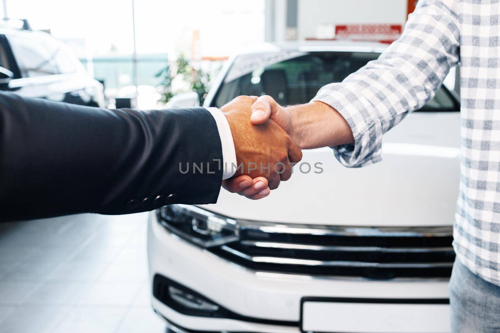 Customer shaking hands with professional car dealer at automobile dealership close up