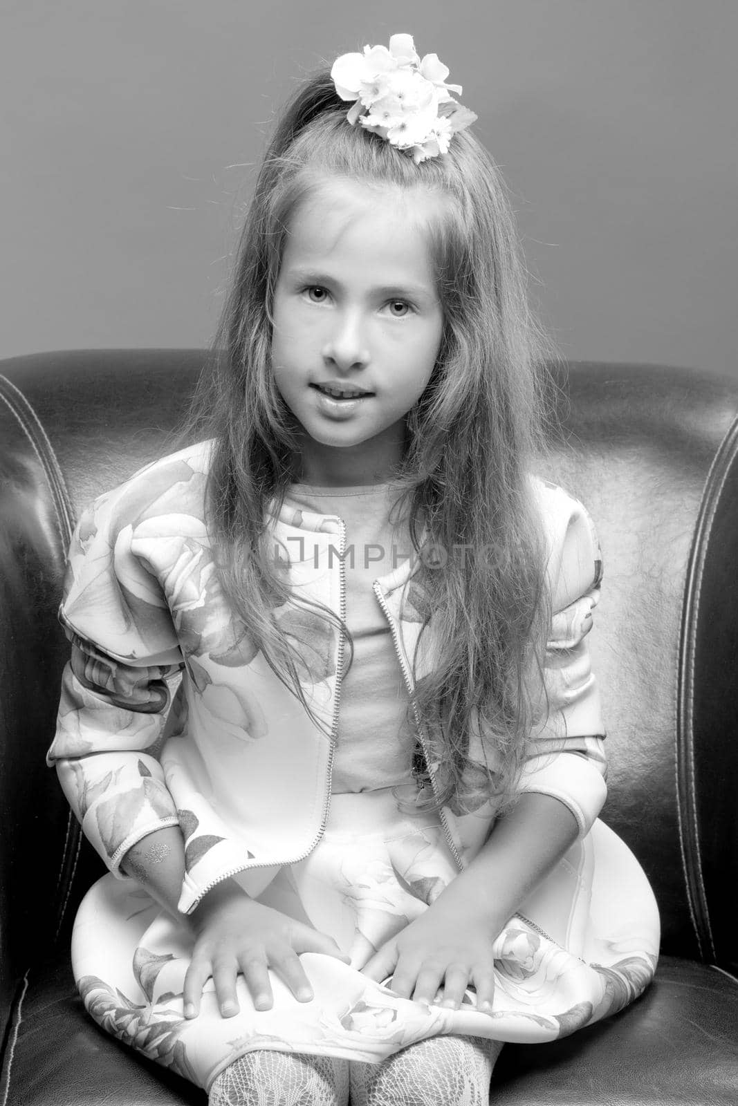 A nice little girl is sitting on a leather chair. The concept of family happiness and home comfort.