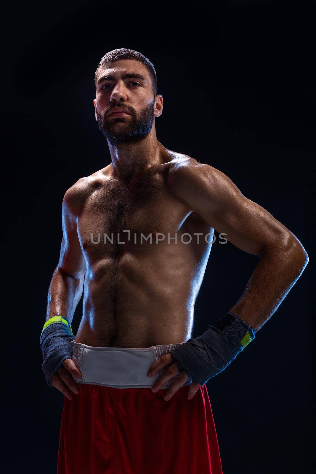Handsome athletic guy in a red shorts on a black background. The boxer is fetching his breath after practicing hooks and blows. Professional fighter. Studio shot