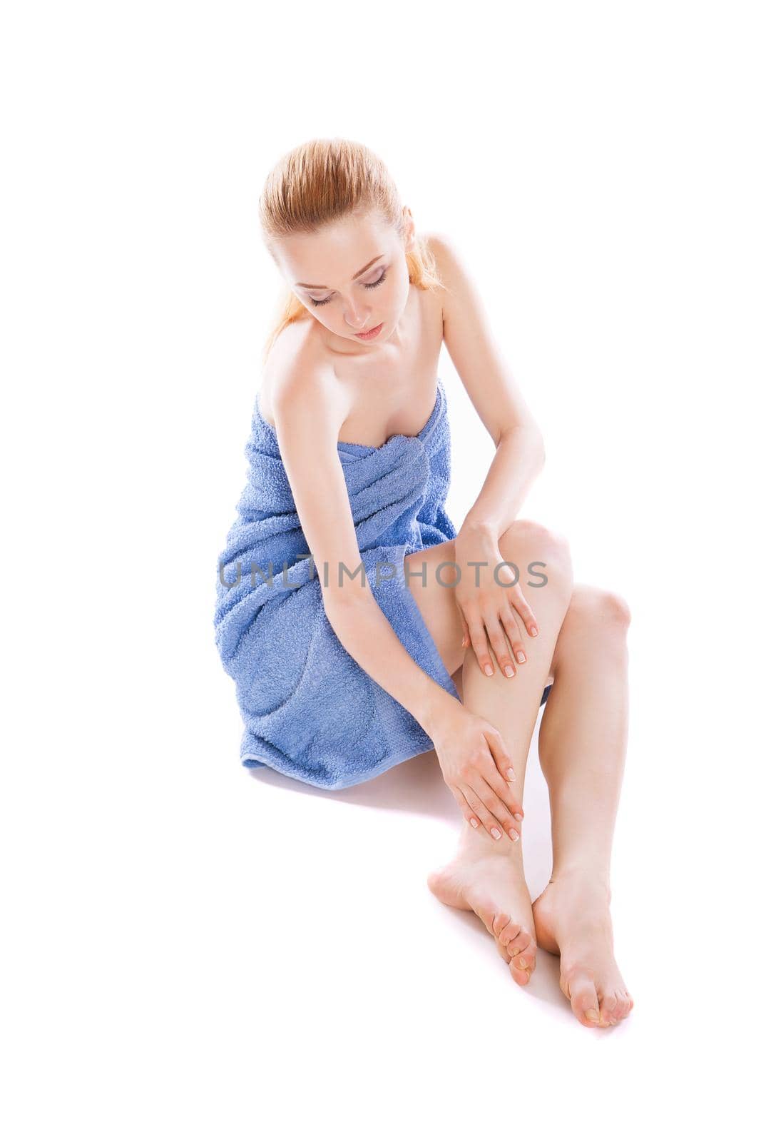 Beautiful young woman in towel sitting on the floor and stroking her beauty legs isolated