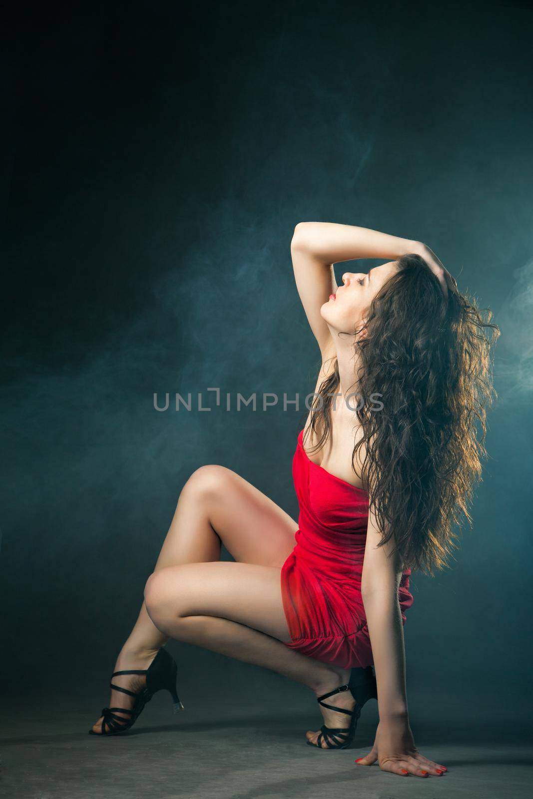 Young sexy dancing woman in red dress with flashes on background with smoke