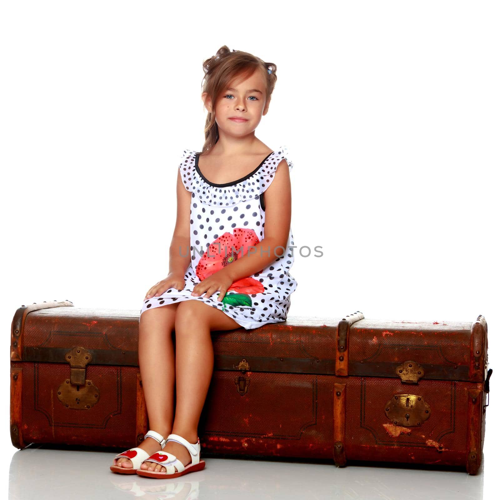 Little girl is sitting on a wooden box. Isolated on white background.
