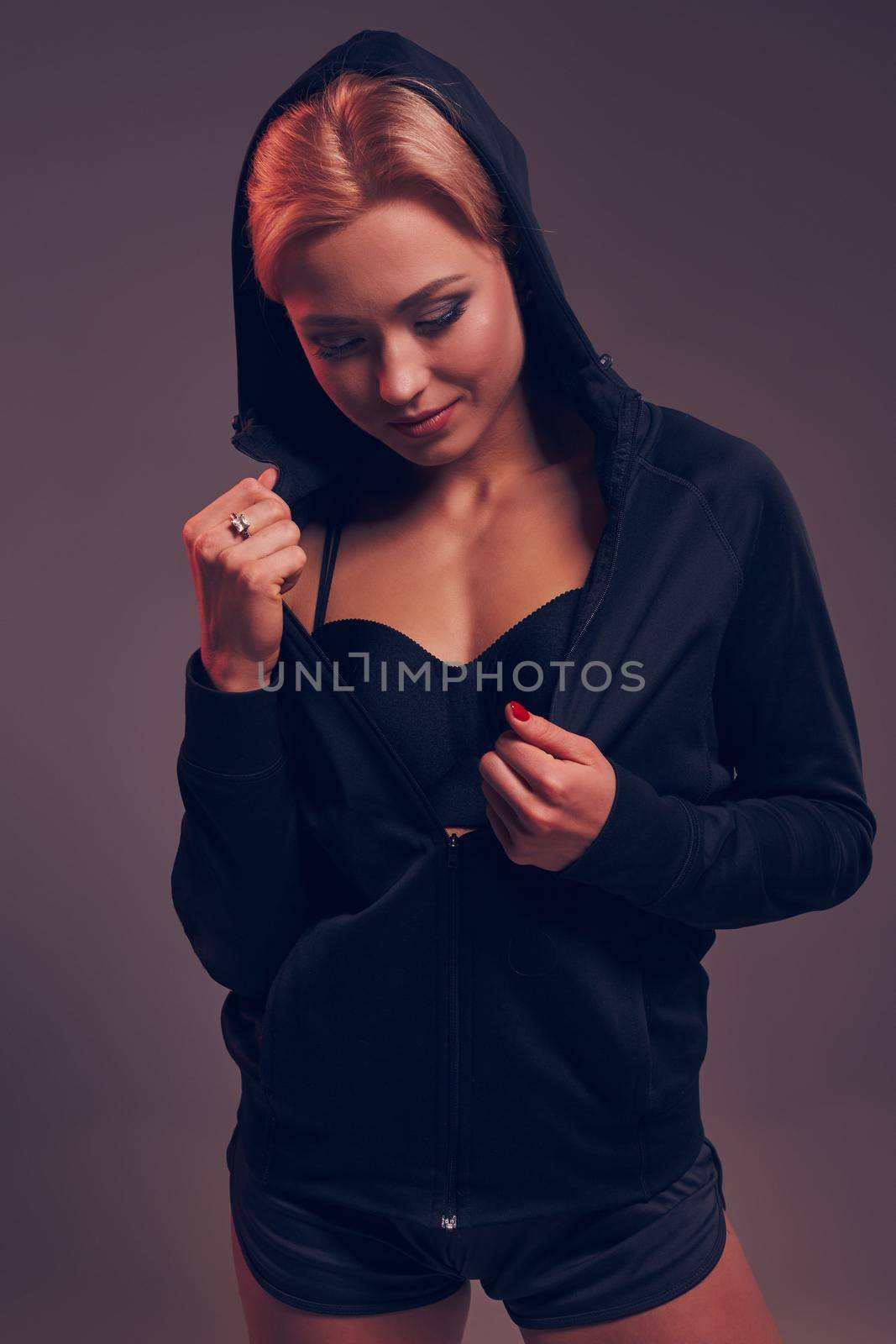 Beautiful seductive sporty girl with the slim sexy figure in the black hoodie, sport underwear and little black shorts is posing in the studio by nazarovsergey