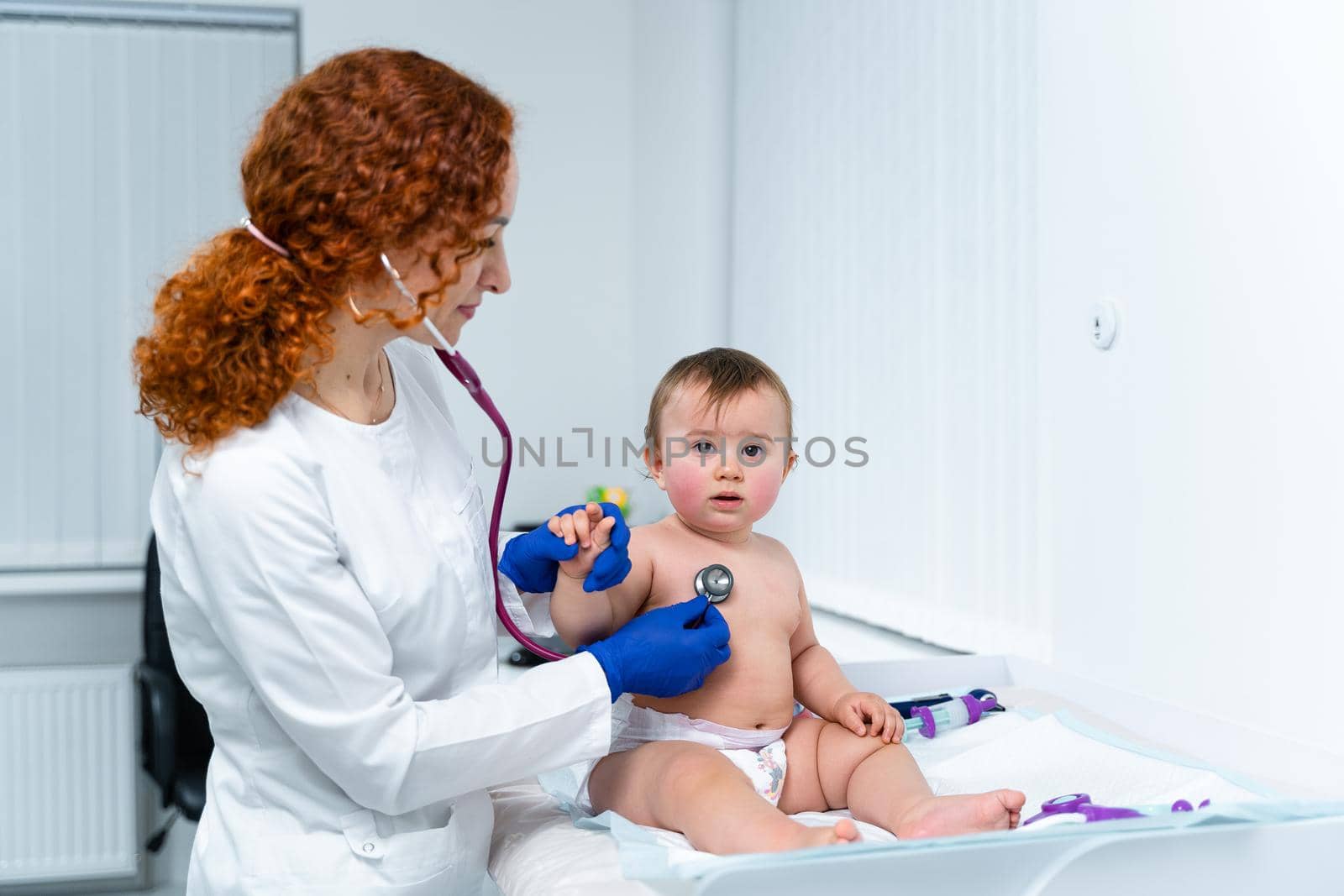 Pediatrician doctor concept. Children medical care. One year old baby girl examined by female pediatrician in clinic office. Child visiting doctor for health check-up. Doctor examine little patient by Tomashevska