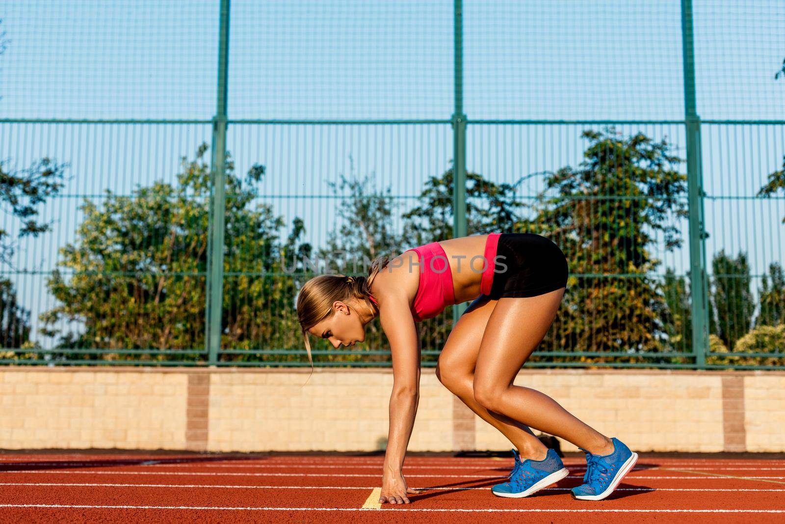 Portrait of beautiful woman ready to start running. Female athlete sprinter doing a fast sprint for competition on red lane at an outdoor field stadium.