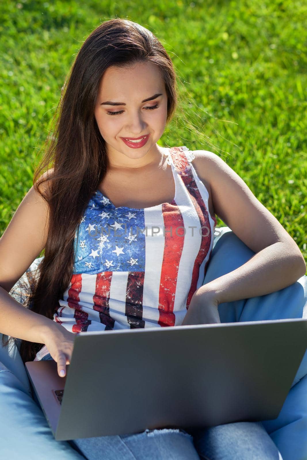 Young cute girl with laptop, sit on bean bag in garden or park, copy space on green grass. Success small business, modern lifestyle, information technology, or online shopping concept