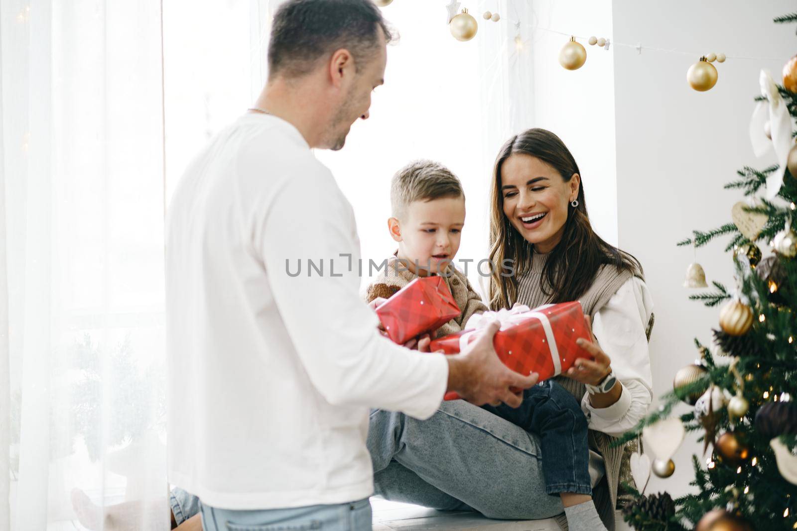 Smiling parents giving Christmas present to son at home by Fabrikasimf