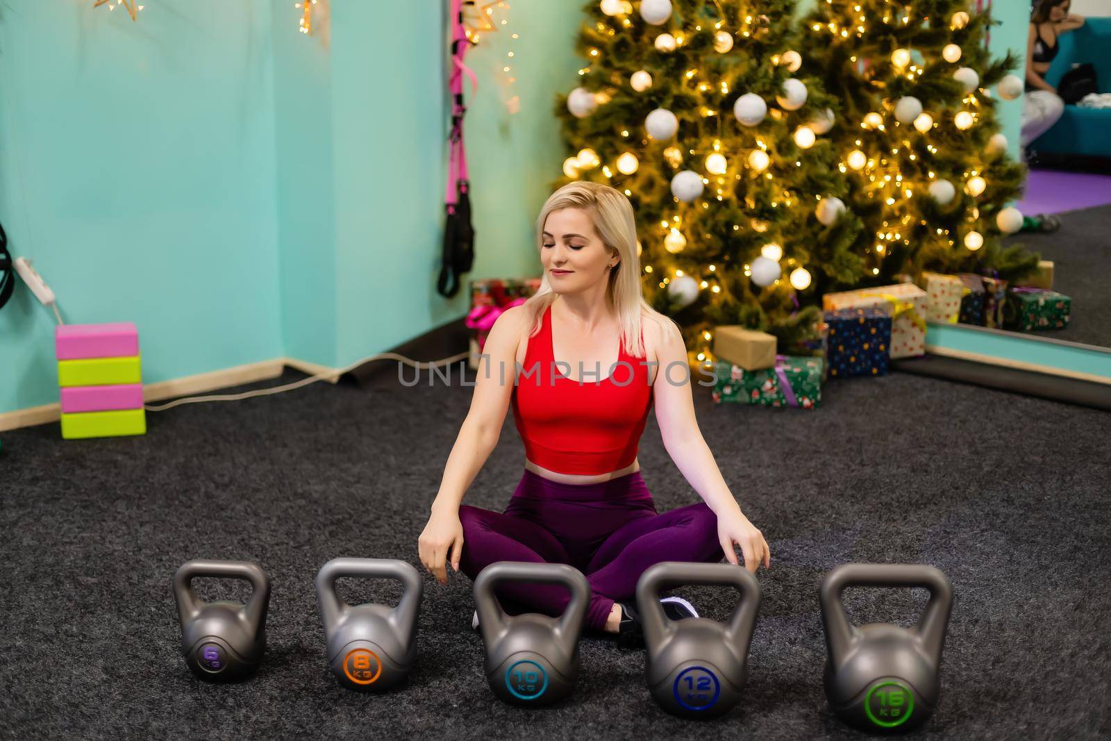 Christmas fitness woman smiling joyful and happy. Beautiful cheerful Caucasian female fitness model near christmas tree at the gym