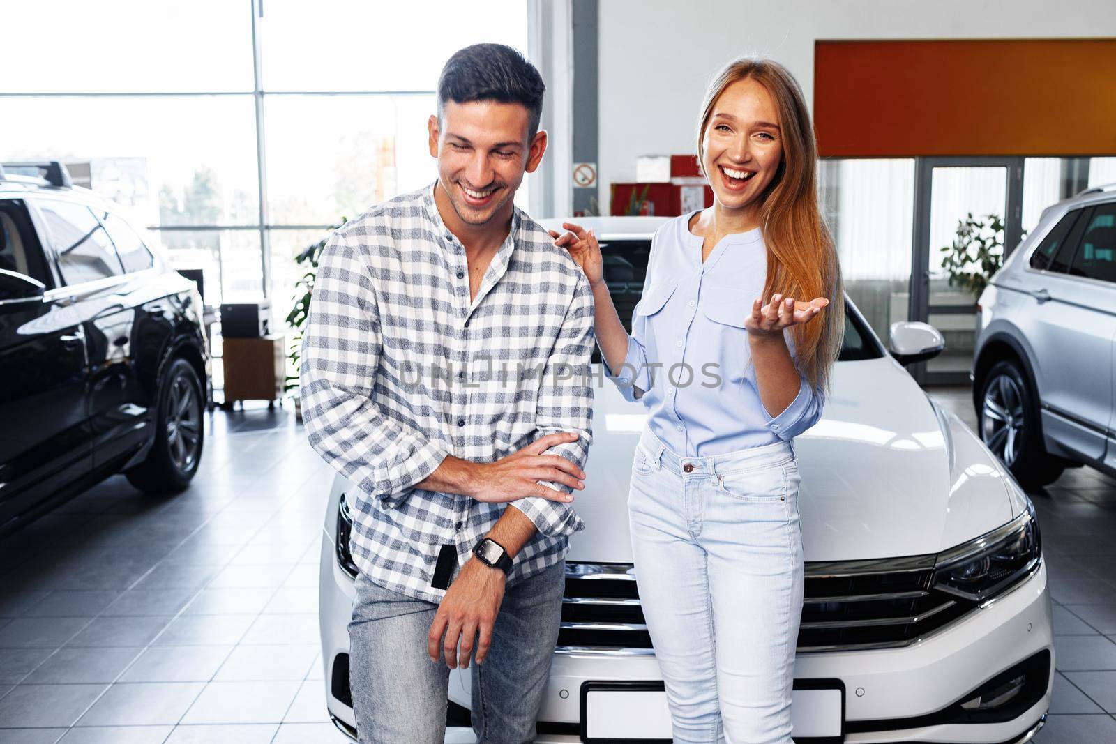 Cherrful young couple at the dealership buying a new car indoors