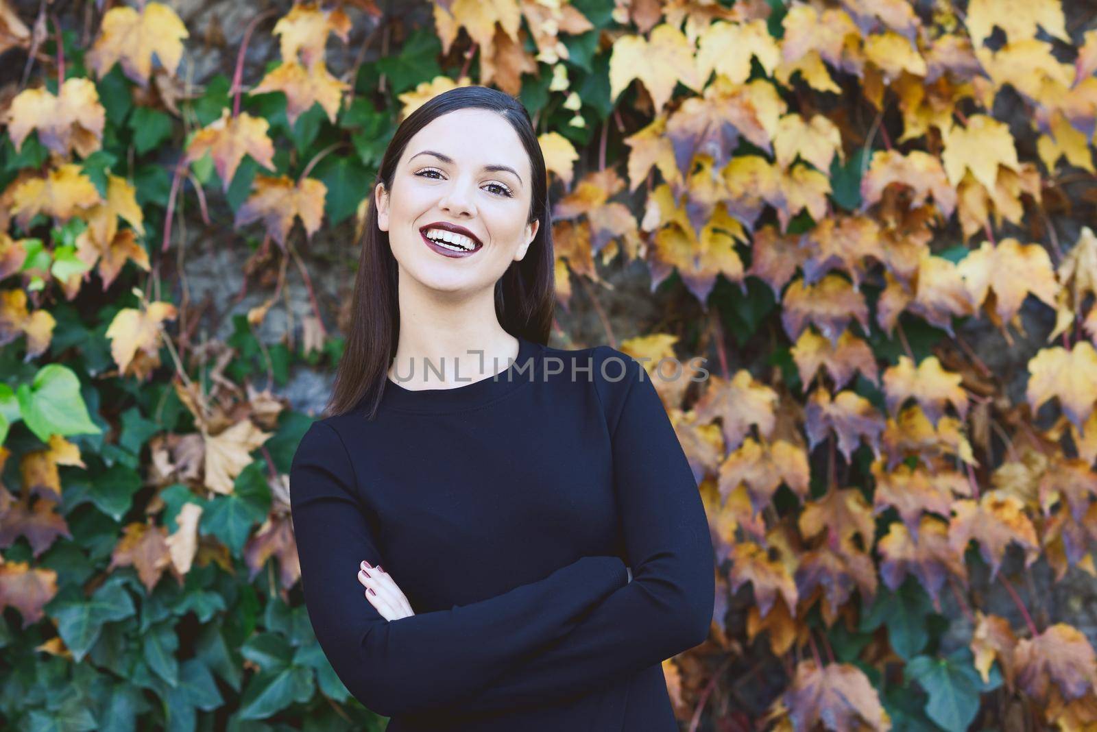 Beautiful young woman, model of fashion, wearing black dress smiling in urban background with autumn colors. Very straight hair styling