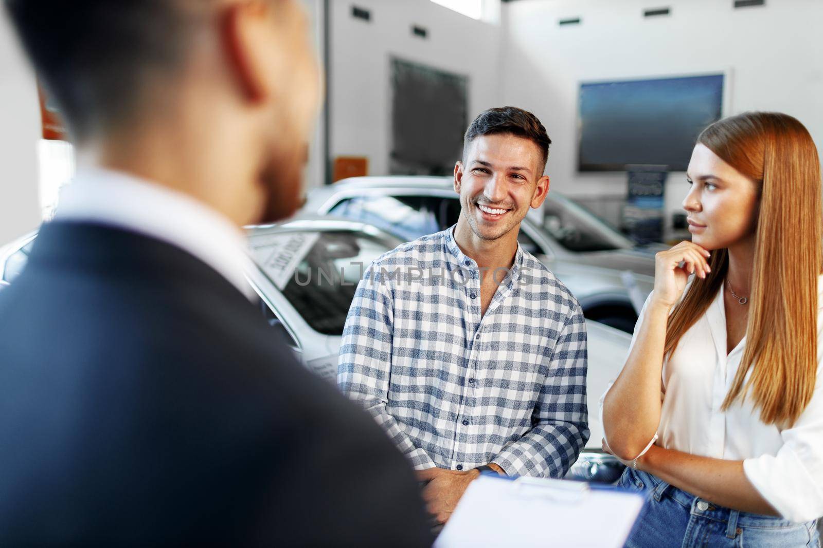 Man car salesman telling about the features of the new car to the couple by Fabrikasimf