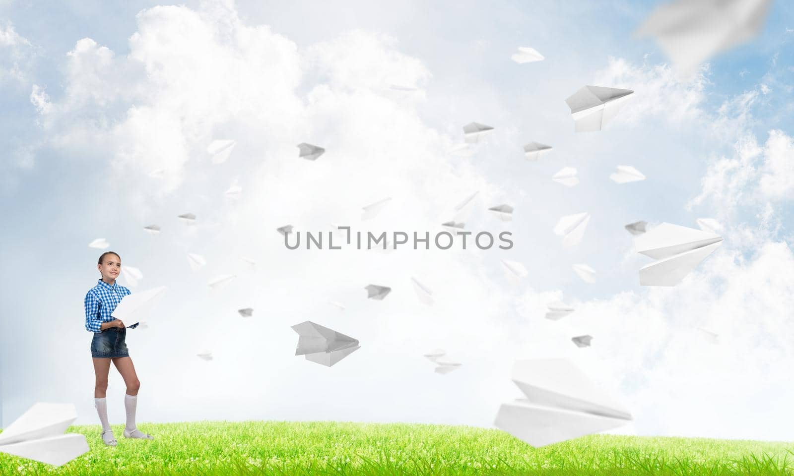 Adorable little girl holding a paper plane outdoors on green grass