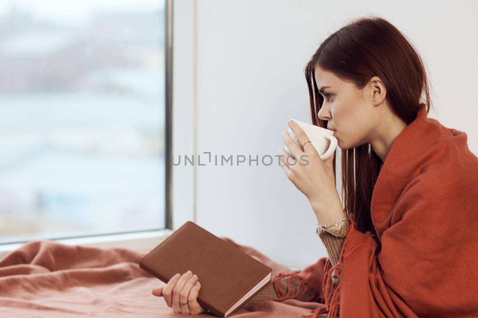 woman with a cup of drink on the windowsill reading a book rest morning. High quality photo