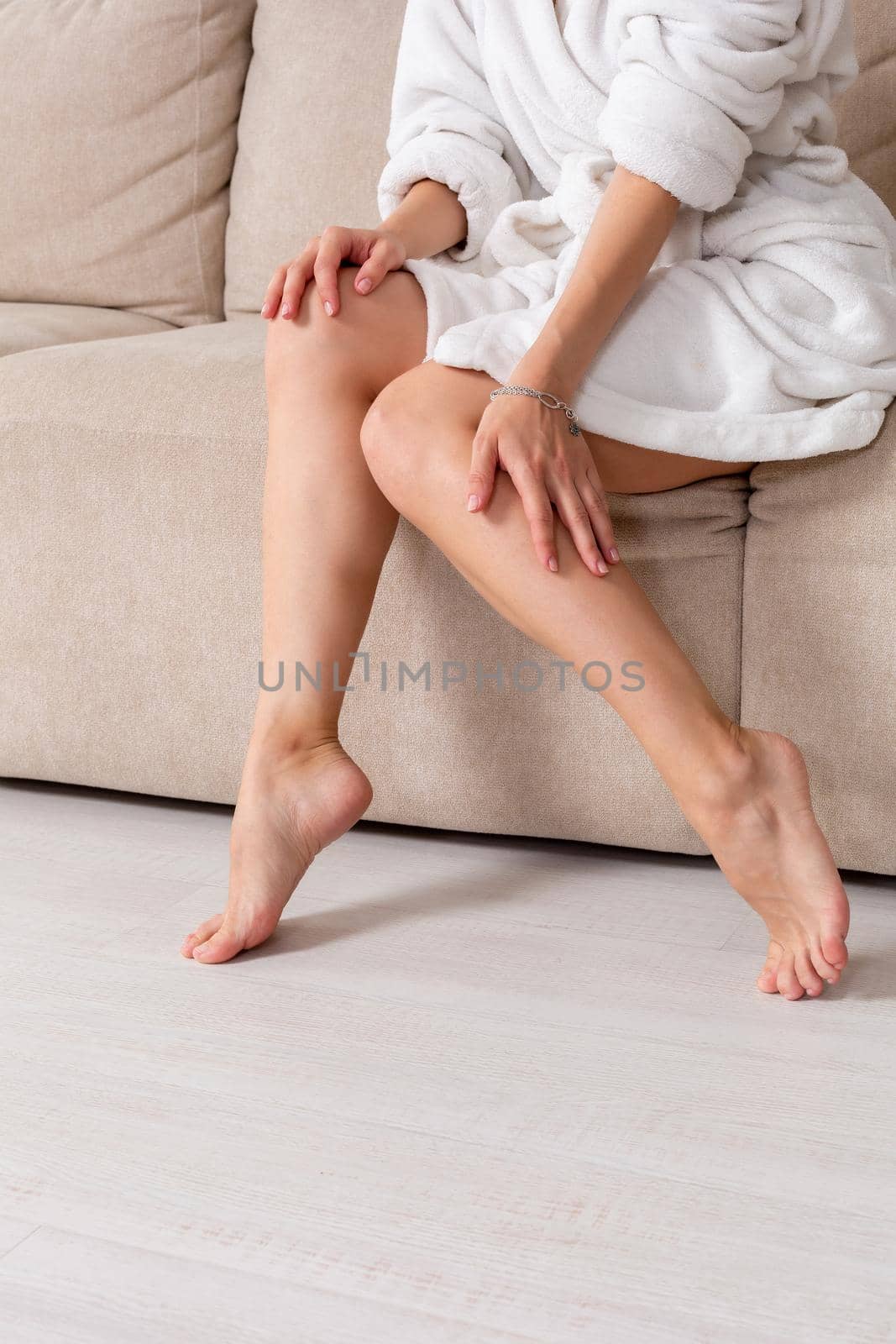 Good morning Close-up of legs of woman in white terry bathrobe on bed with ideal figure in light room. Charming woman relaxing in hotel room