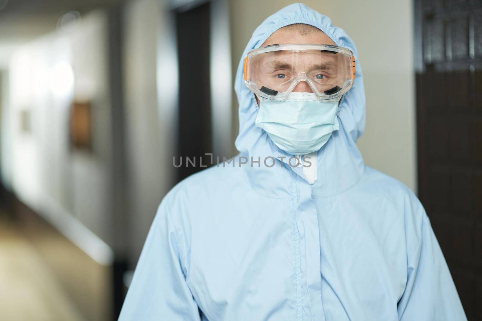 Waist up of worker in protective clothing and suit standing in the hotel corridor. Coronavirus and quarantine concept