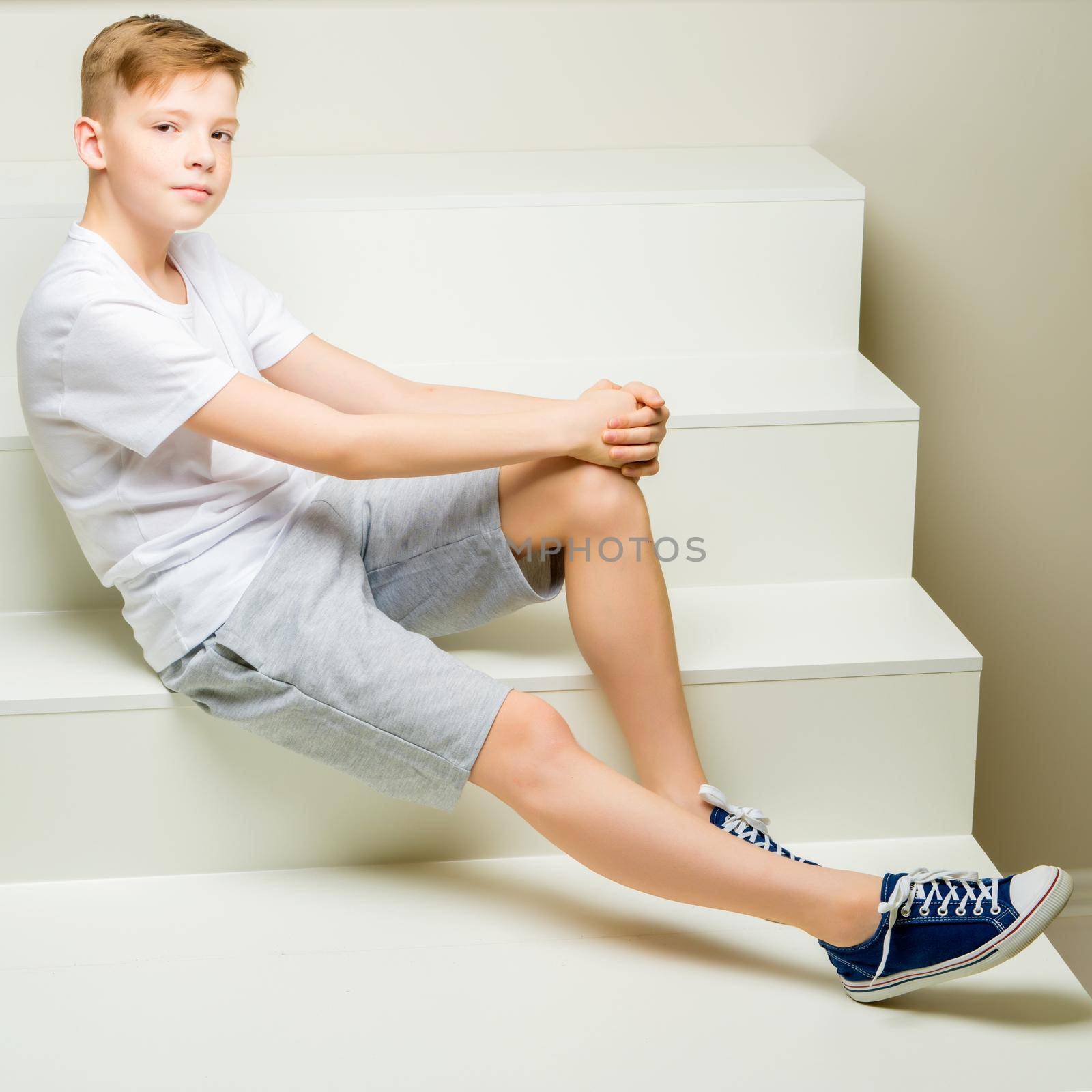 A handsome school-age boy sits on a white staircase. The concept of youth culture.