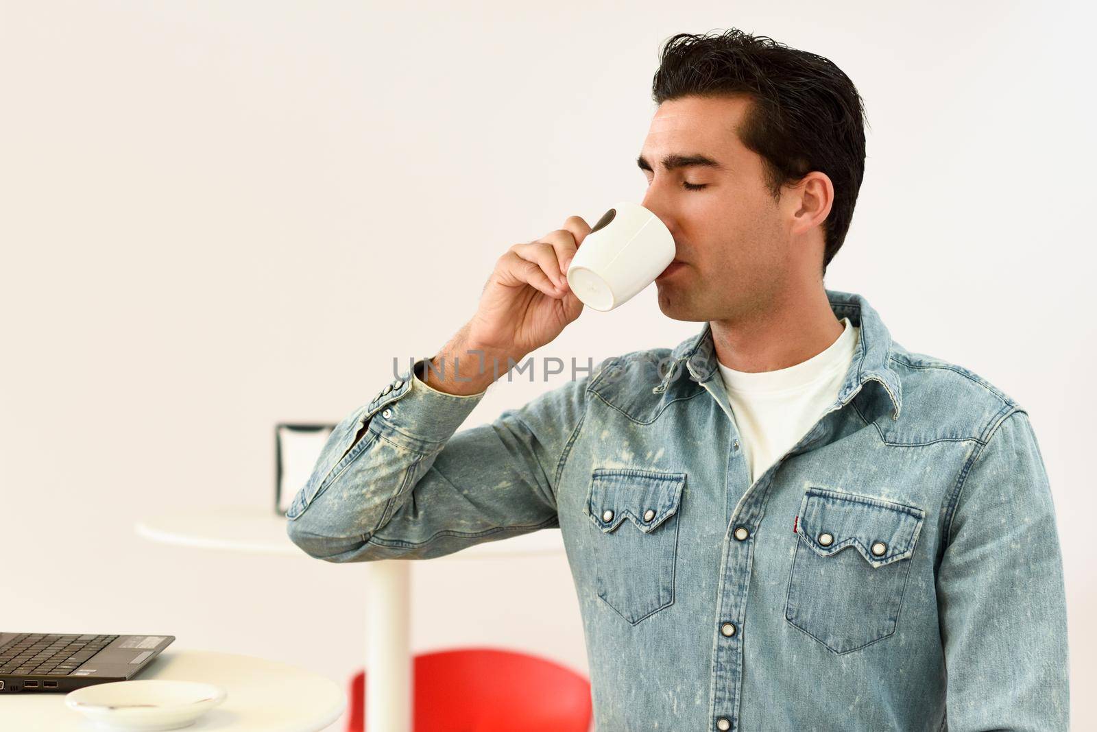 Good looking man wearing denim shirt sitting in a coffee bar. Blue eyes guy with casual clothes.