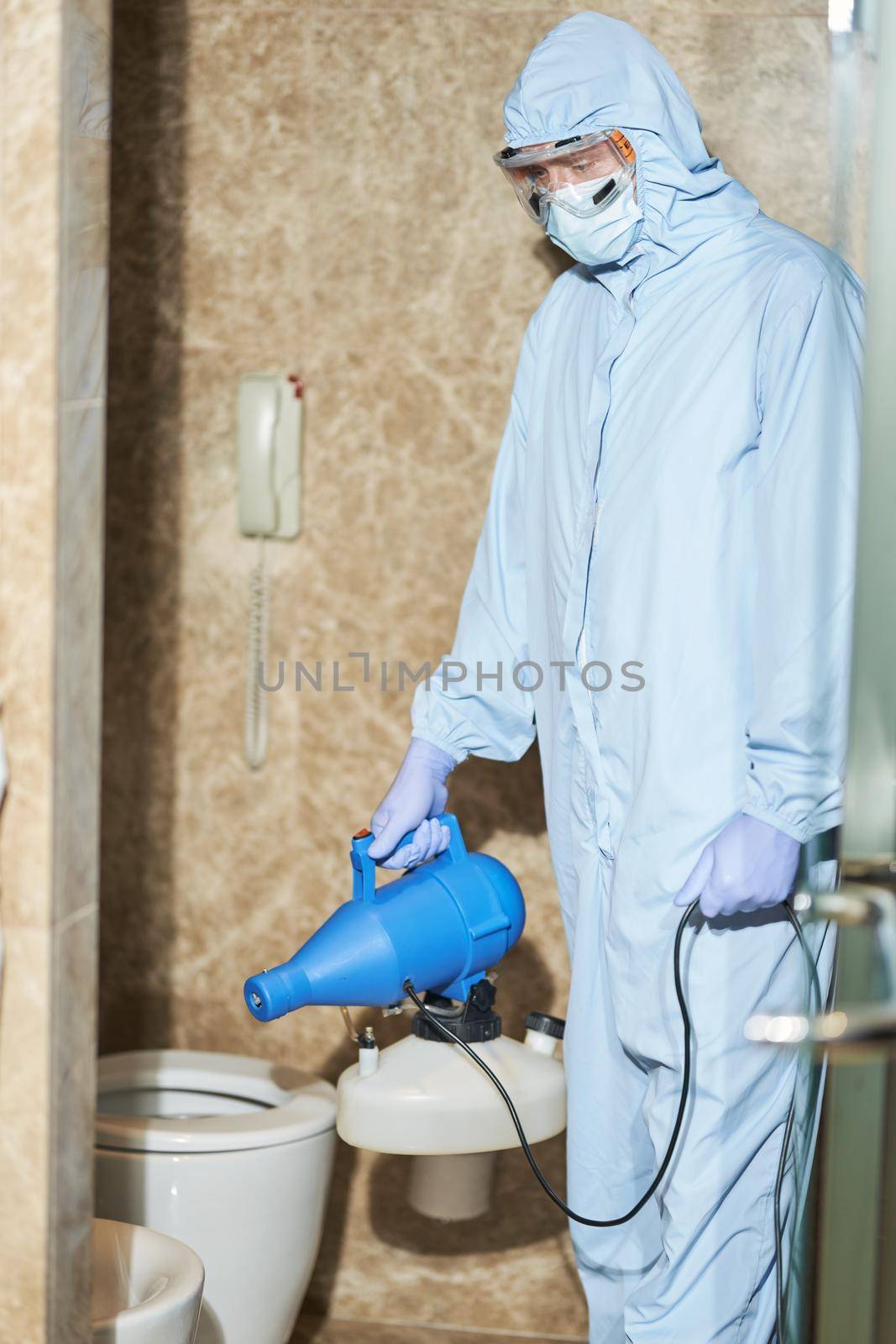 Male worker wearing suit to protect against COVID-19 using nebulizers in hotel bathroom. Coronavirus and quarantine concept