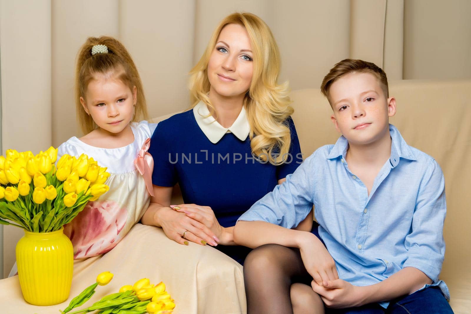Mom and son and daughter are sitting on the couch in the studio. by kolesnikov_studio