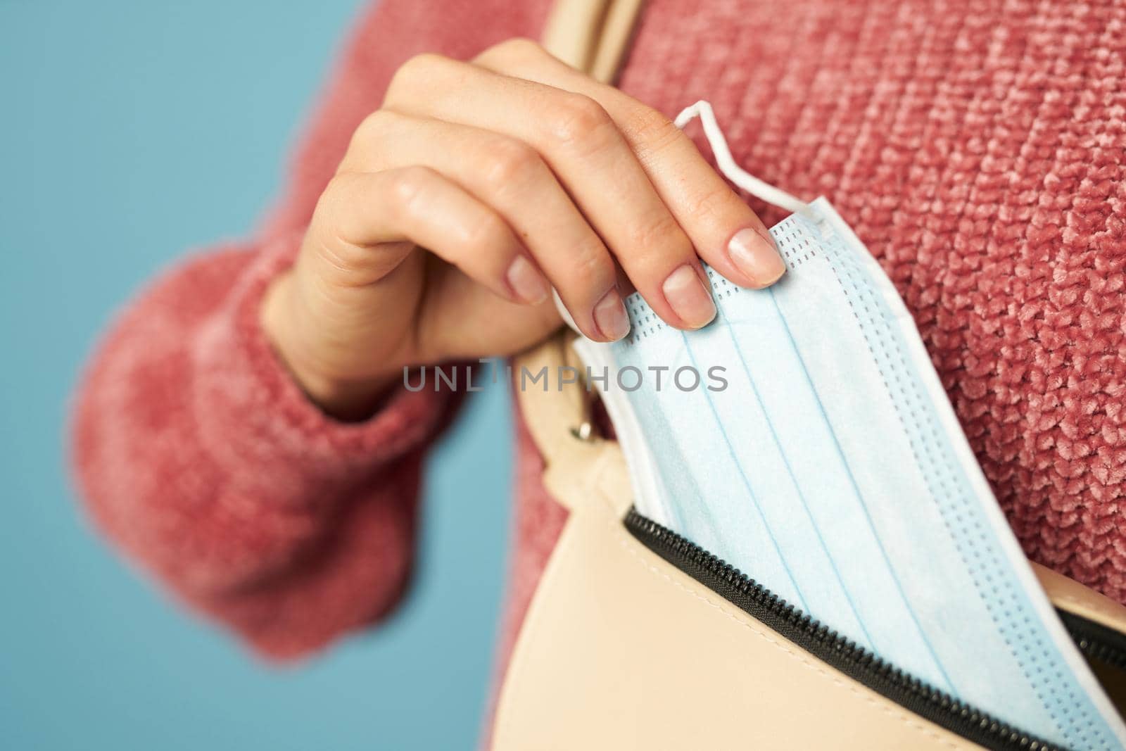 Young woman wearing a sweater holding a face mask in studio by friendsstock