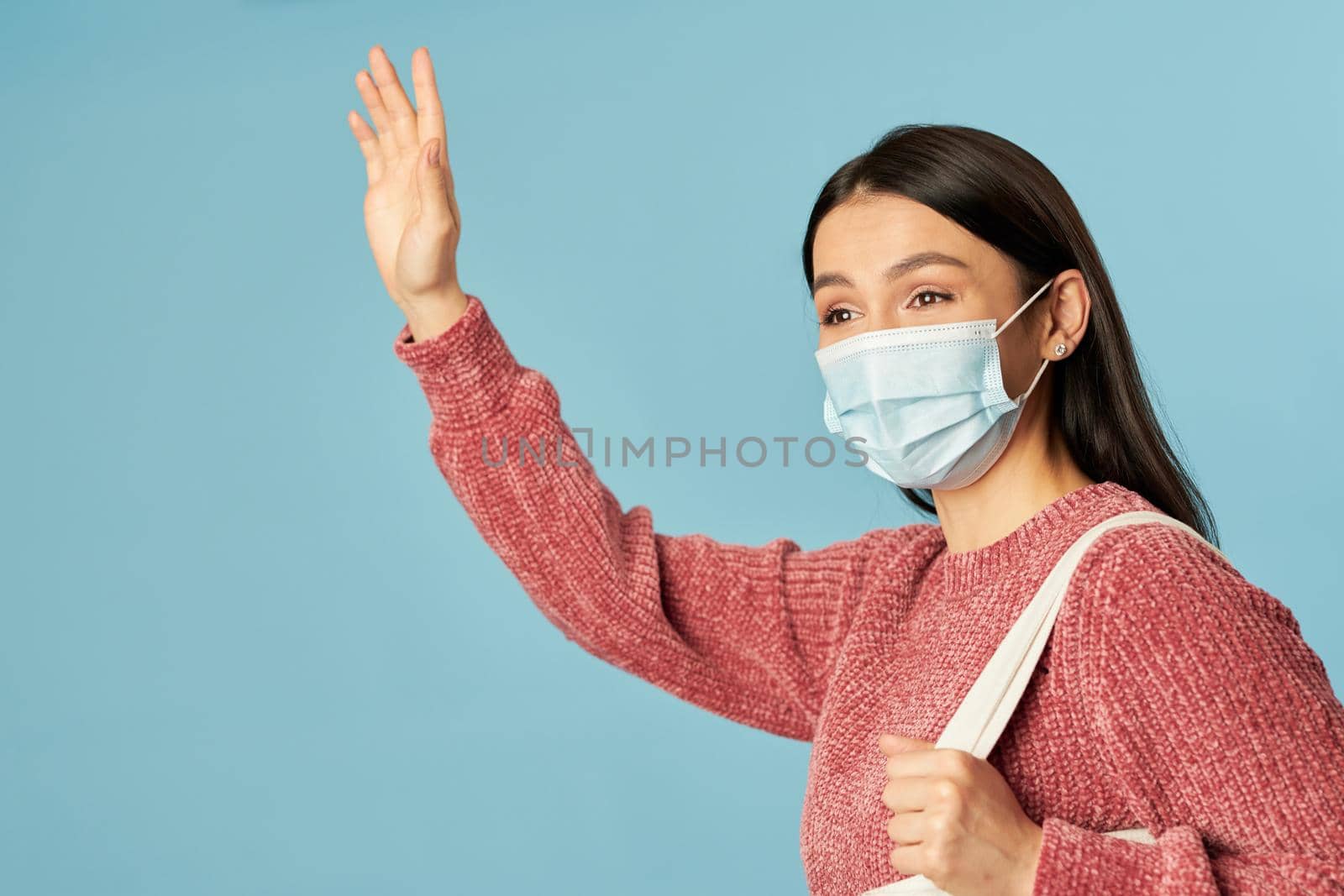 Waist up of beautiful young woman waving hand while wearing face mask and holding shopping bag. Copy space. Quarantine, coronavirus concept