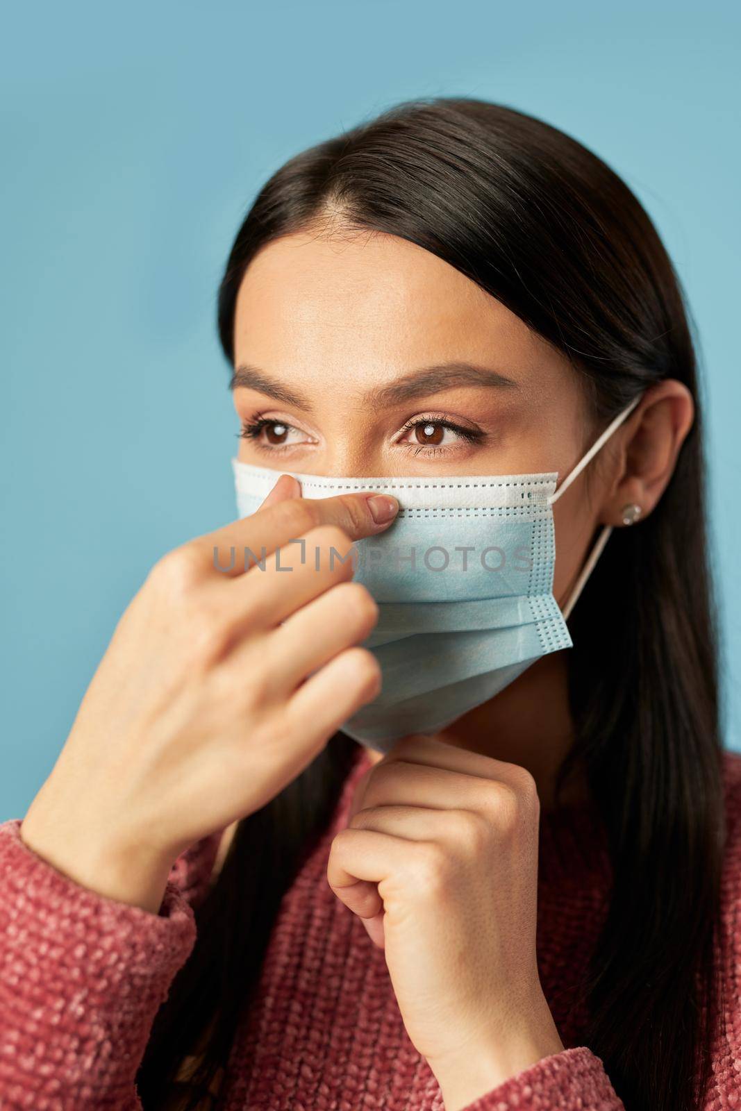 Portrait of pretty female standing in studio and wearing protective face mask, isolated on blue background. Copy space. Quarantine, coronavirus concept