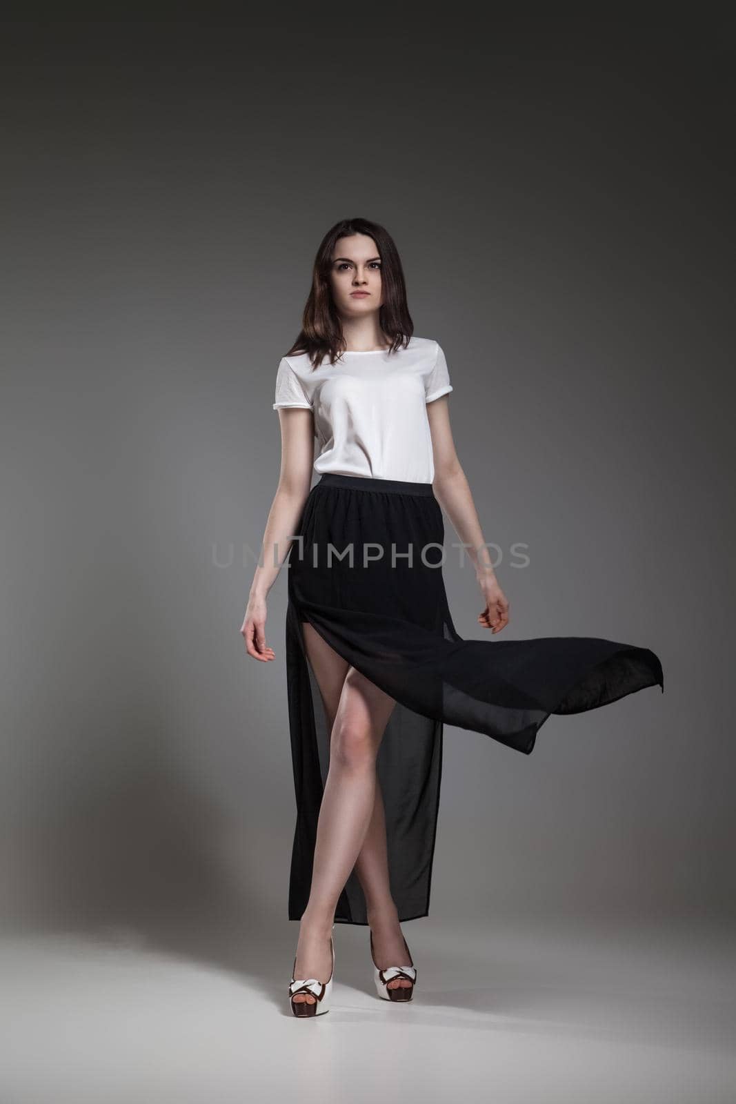 Beautiful model in white blouse and black skirt posing on grey background