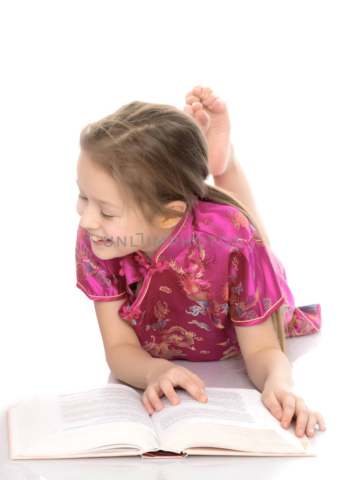 A little girl is lying on the floor reading a book. Conception Happy childhood, family and people, training and education, harmonious development of the child in the family. Isolated on white background.