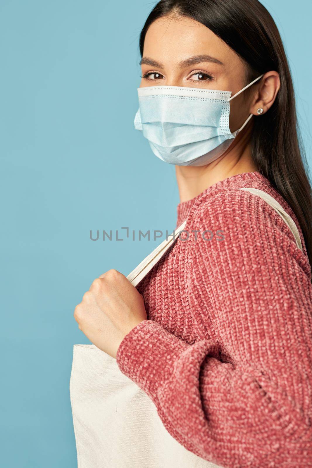 Side view of pretty woman in disposable face mask holding shopping bag. Copy space. Quarantine, coronavirus concept