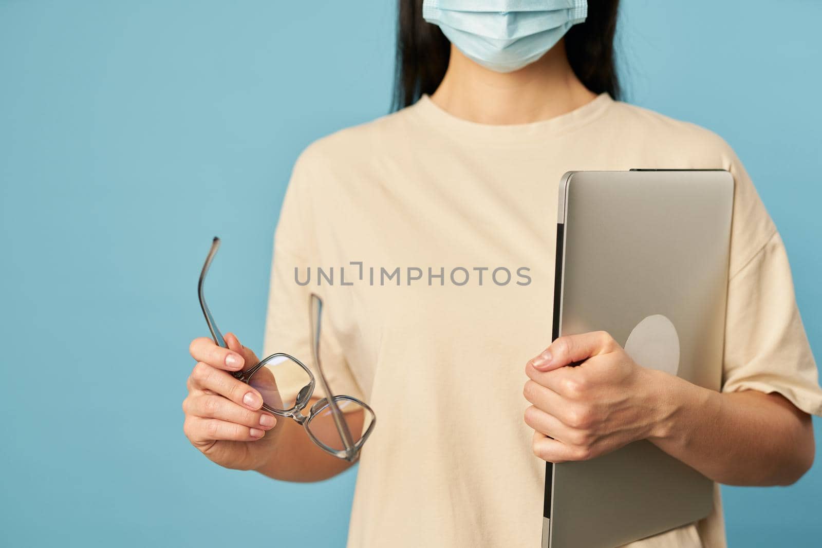 Cropped photo of woman holding glasses and gadget while posing in studio, isolated on blue background. Copy space. Quarantine, epidemic concept