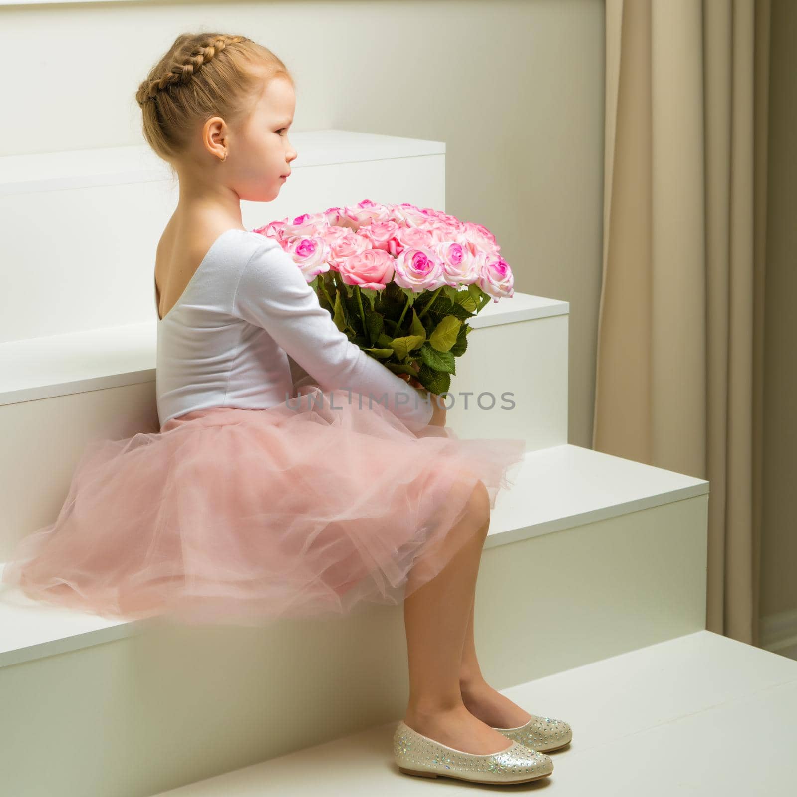 A cute little girl with a bouquet of flowers sits on a white staircase. The concept of happy people, childhood.