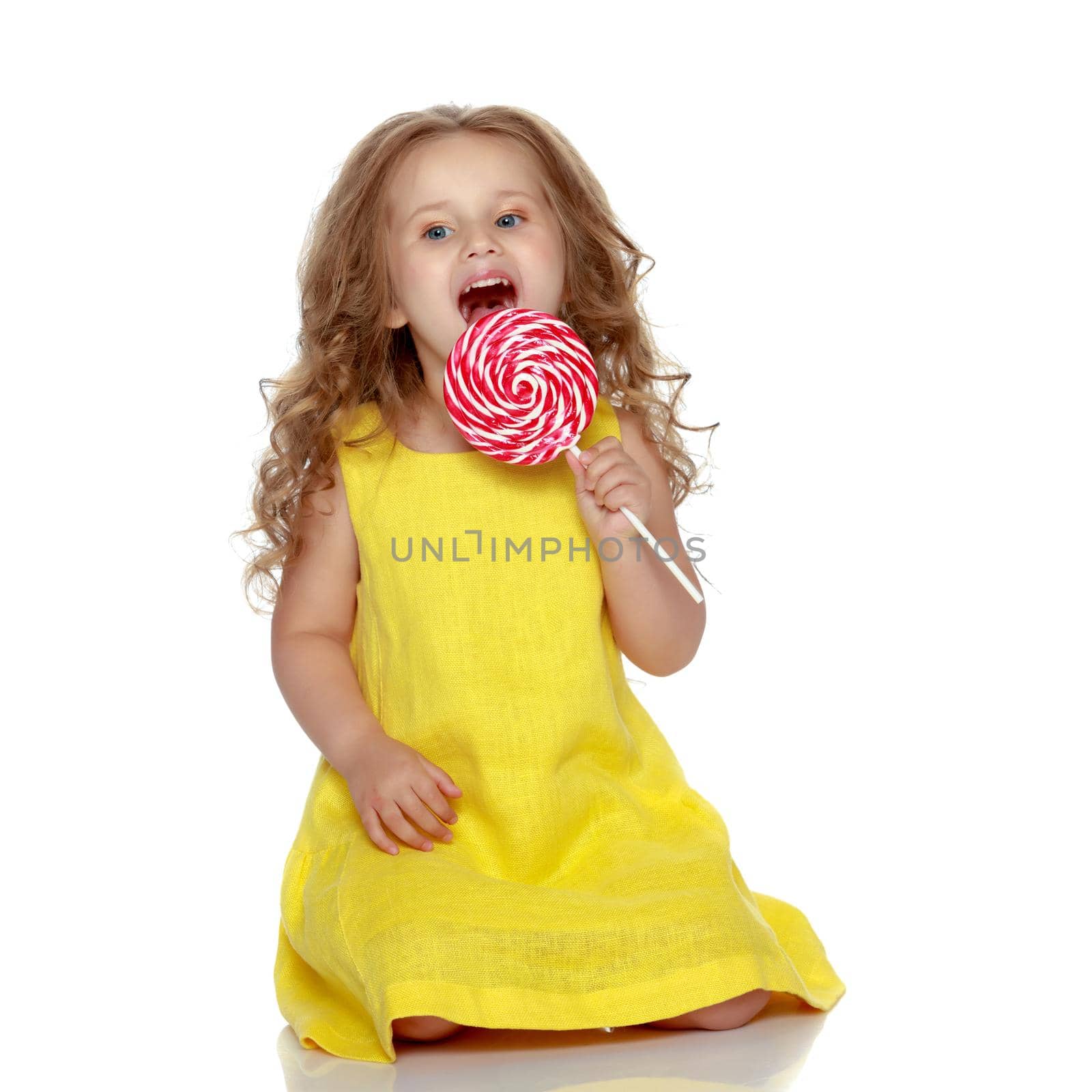 A little girl licks a candy on a stick. Isolated on white background.