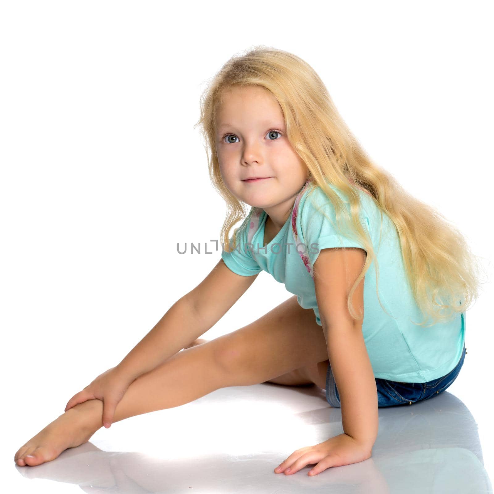 Beautiful little girl is sitting on the floor in the studio. The concept of a happy childhood, beauty and fashion. Isolated on white background.