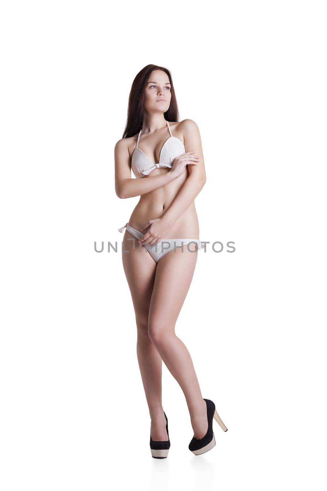 Portrait of a beautiful brunette girl wearing white bikini posing at studio