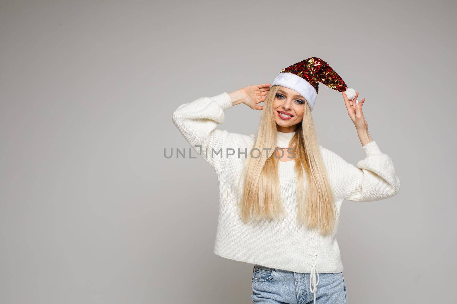 caucasian girl with long fair hair in white sweater, blue jeans and red christmas hat