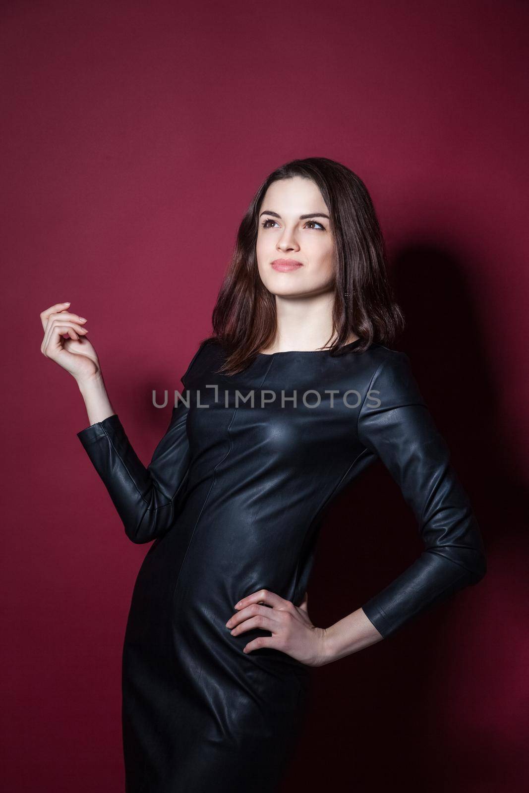 Young beautiful model posing in leather dress on red background