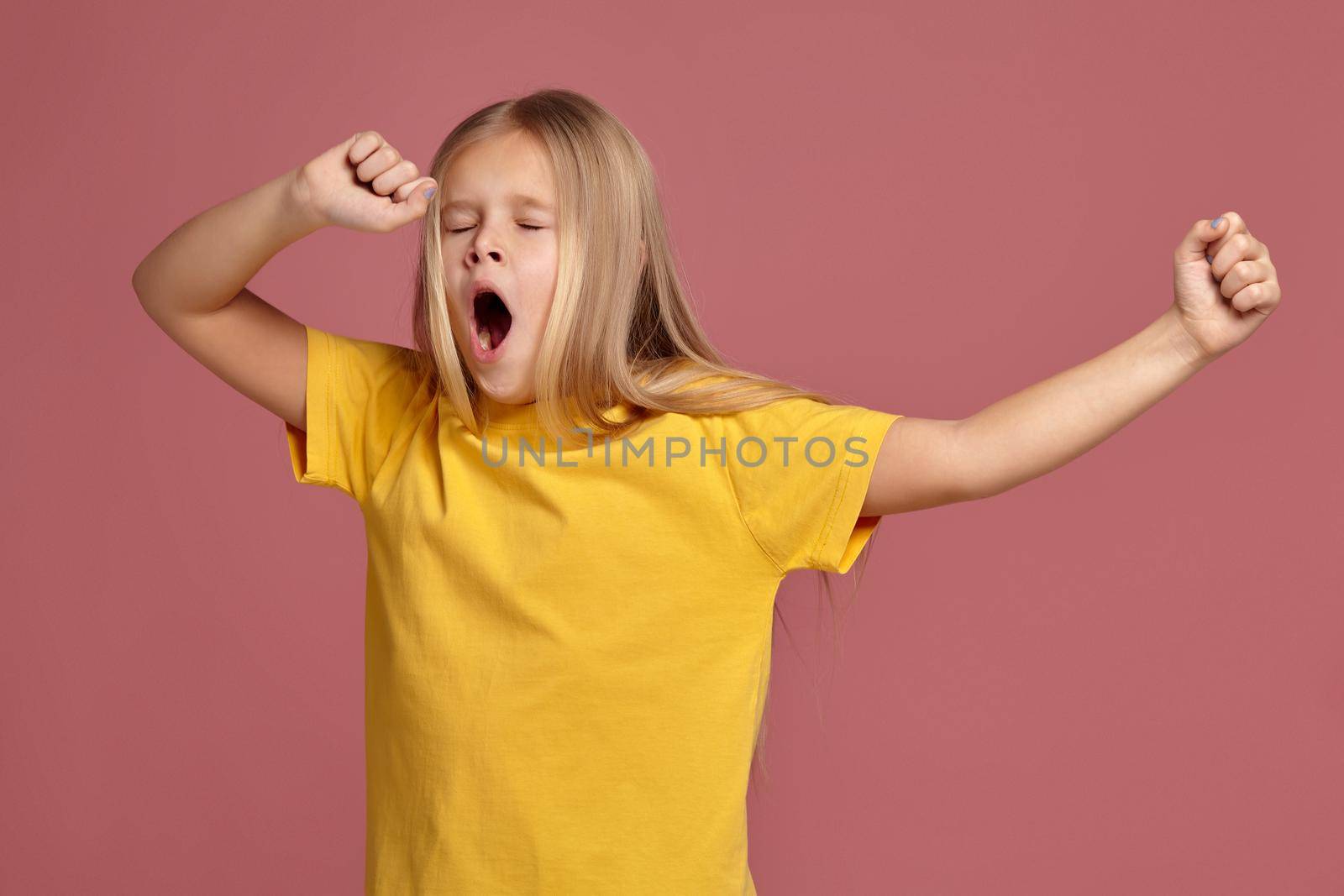 little girl in a yellow T-shirt on a coral background. stretches and yawns