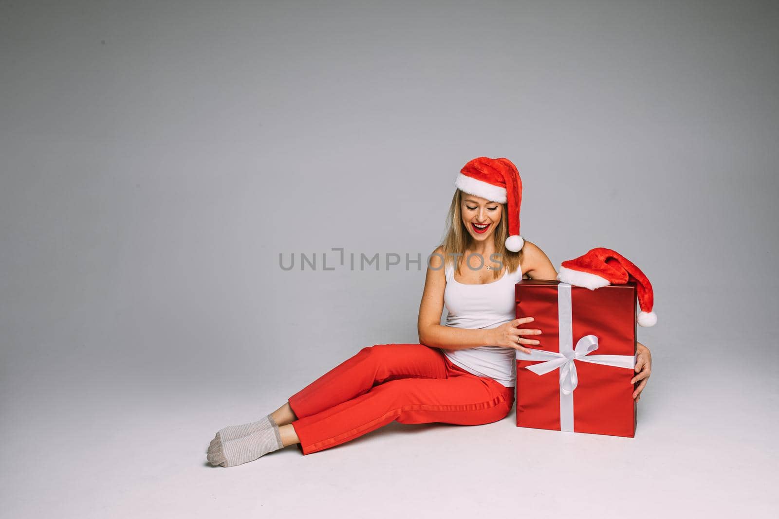 Pretty woman in Santa hat posing with Christmas present box by StudioLucky