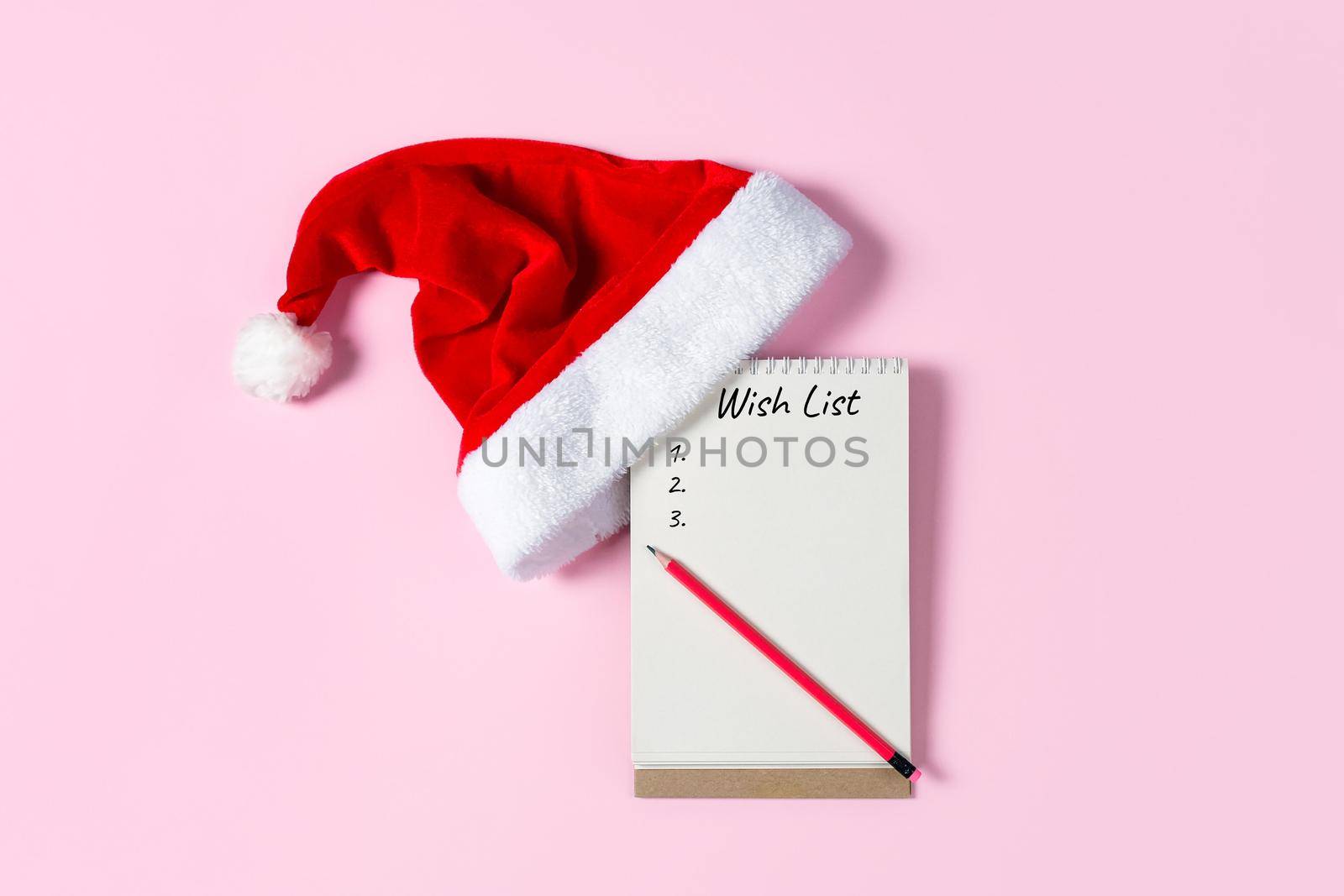 New Year or Christmas wish list concept. Notepad, Santa Claus hat isolated on pink background. Holiday banner with copy space.