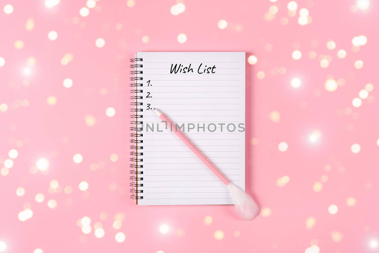 New year, Christmas or holiday wish list concept. Notepad and golden tinsel isolated on pink background. Holiday Banner with copy space.