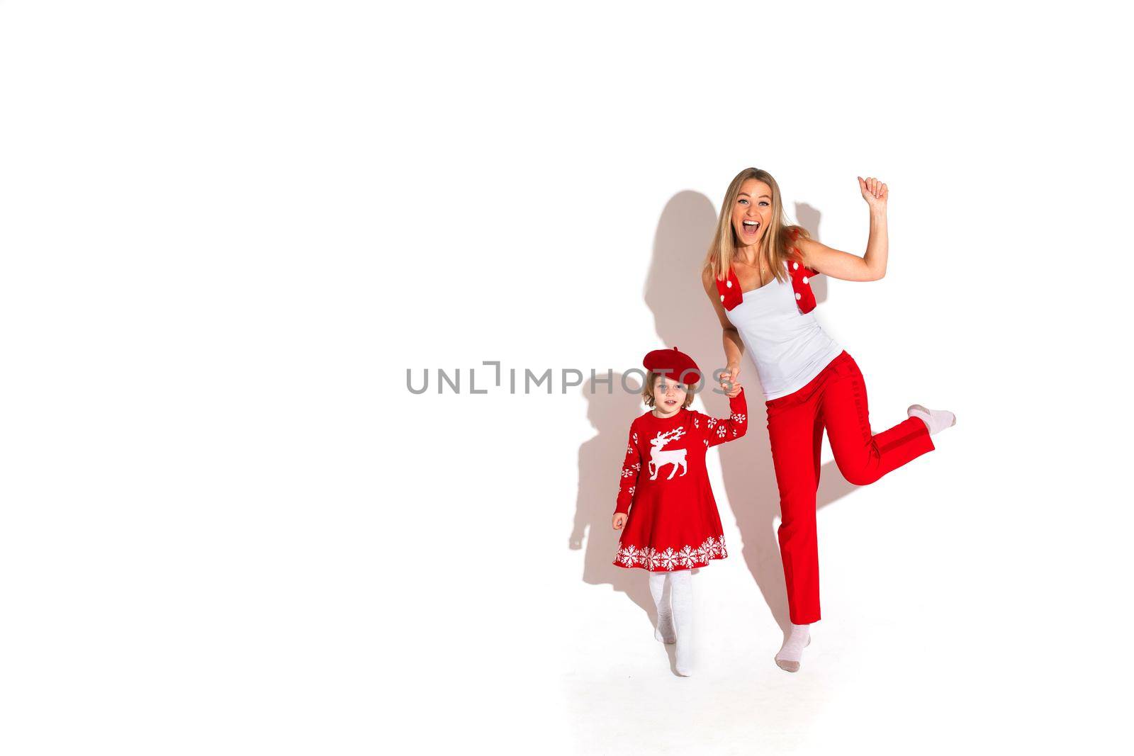 Christmas concept photo of little girl in red dress holding hands with an excited blonde woman while waving at the camera