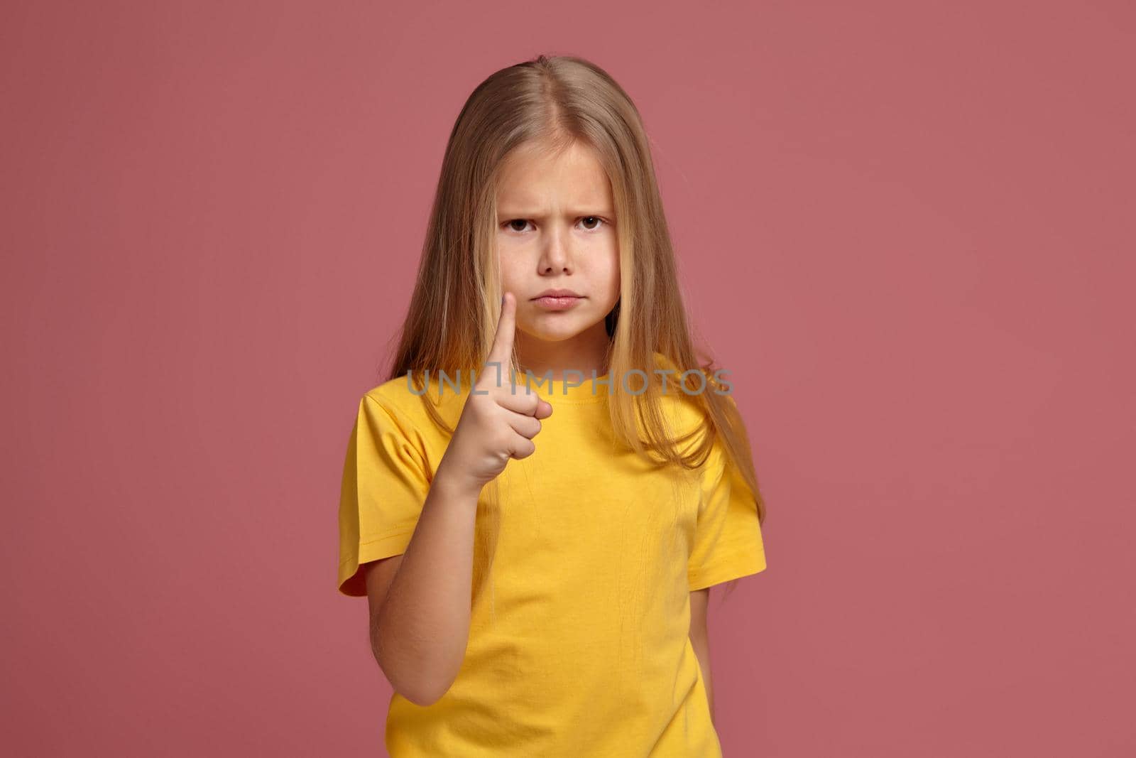little girl in a yellow T-shirt on a coral background. points finger