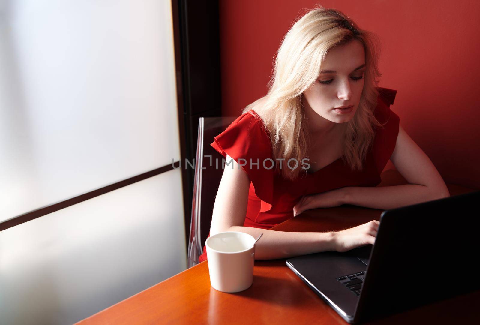 Young adult woman wearing red jumpsuit and using laptop by Novic